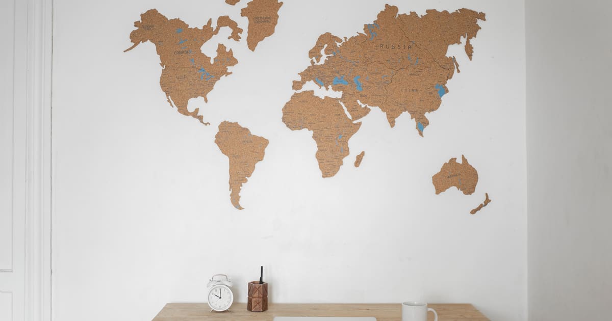 A travel agency workspace with a cork world map on the wall above a light wooden desk with a clock