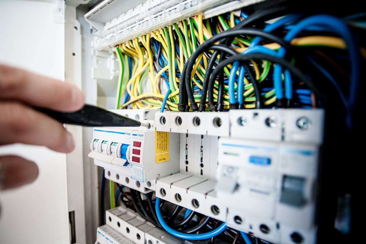 Close-up of an electrician's hand working on a colorful-wired circuit breaker panel